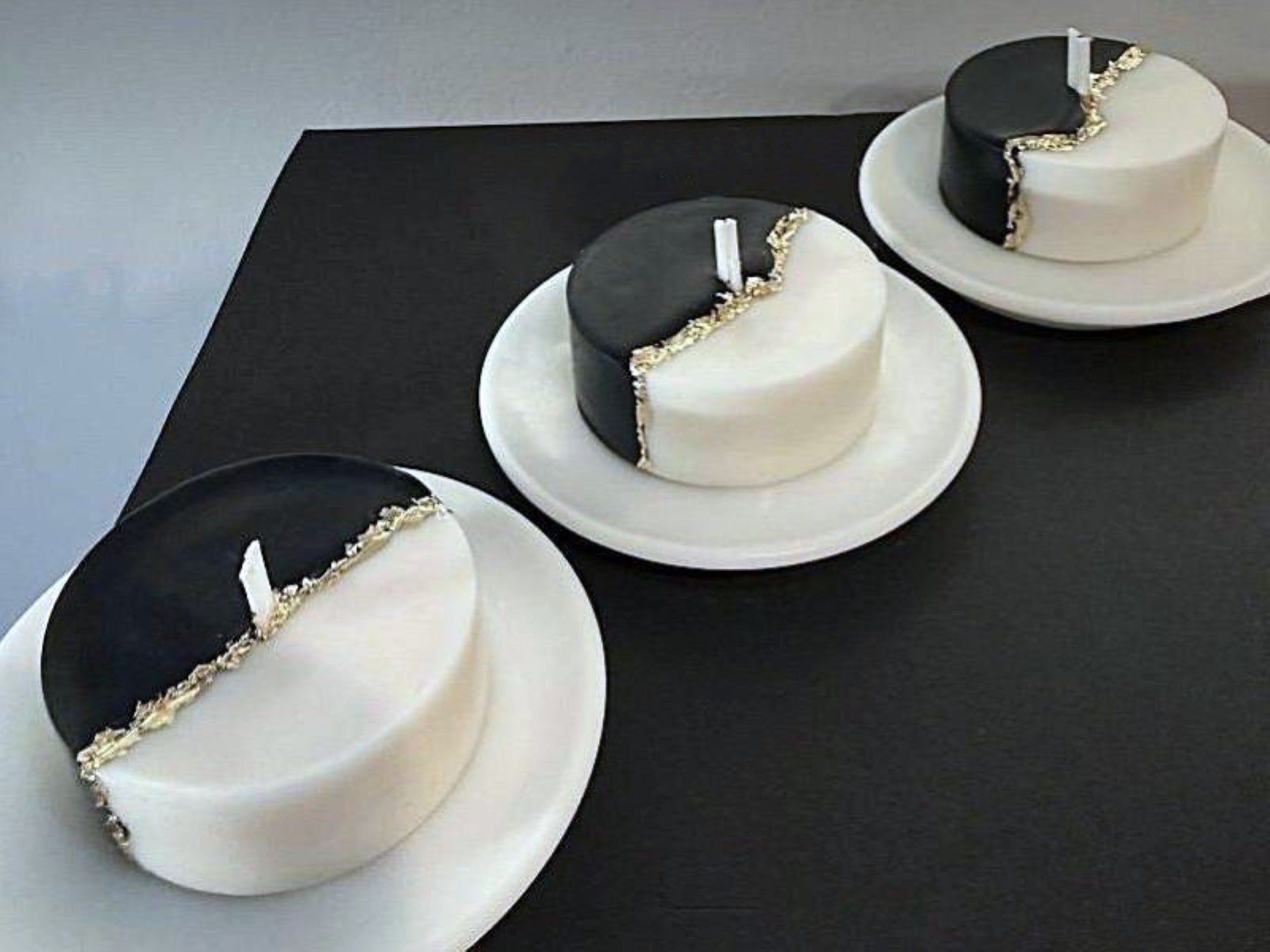 Three black and white candles with gold accents on a dark surface.