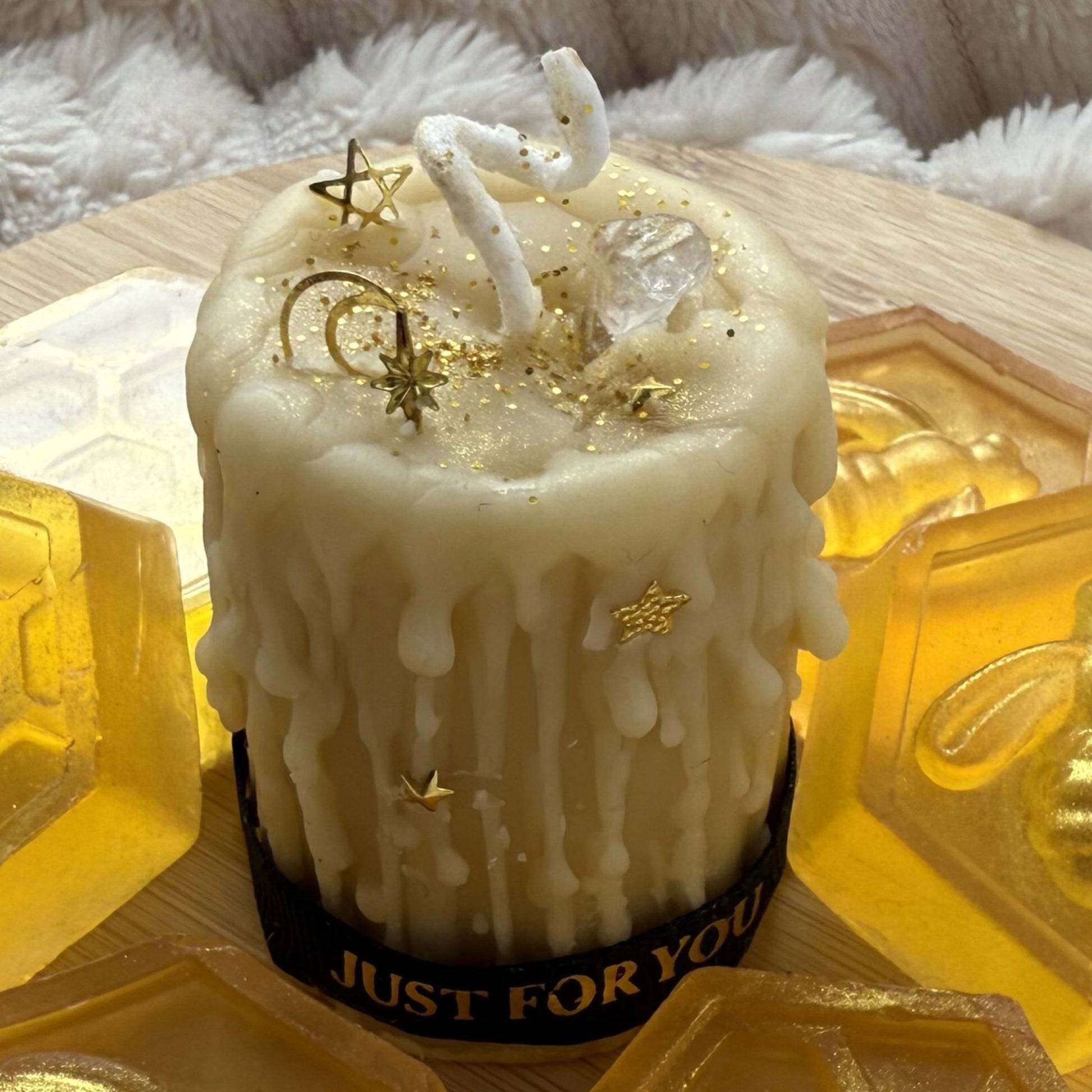 Beeswax candle with gold stars and 'JUST FOR YOU' ribbon on a textured surface.